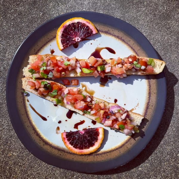 Two bruschetta slices with diced tomatoes, onions, and greens, garnished with blood orange slices and balsamic glaze.
