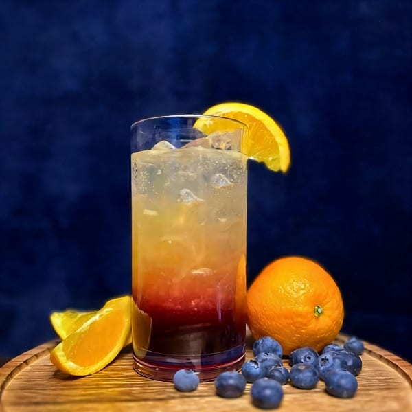 Layered orange and red drink with ice, garnished with an orange slice, blueberries, and oranges.
