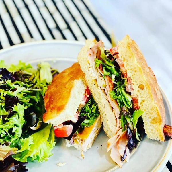 A Hidden Julles breakfast sandwich with ham, lettuce, and tomato, served with a side salad.