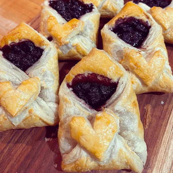 Several blueberry danishes with heart-shaped pastry accents on a wooden surface.